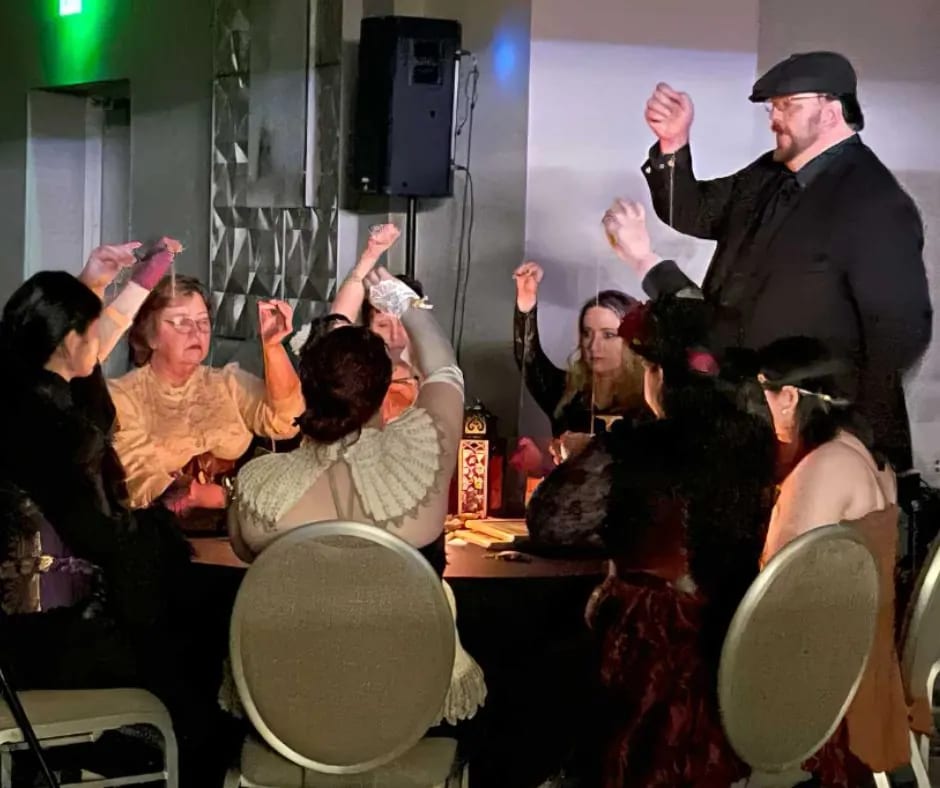 Guests in Victorian dress holding pendulums aloft during a séance led by Vince Wilson