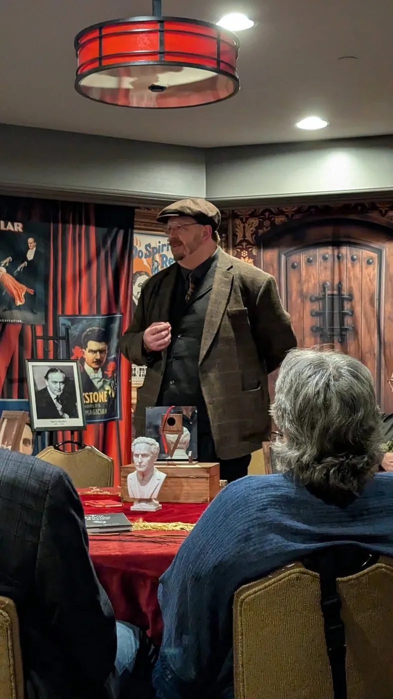 Vince Wilson presenting a Houdini séance beside a bust and portrait of Harry Houdini and vintage magic posters